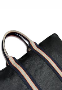 Zwarte leren tote bag met twee brede navy, witte en oranje gestreepte stoffen handvatten tegen een witte achtergrond.
