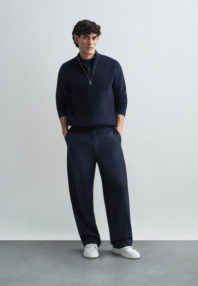 Navy ribbed knit pullover with a half-zip collar, paired with navy pinstriped wide-leg trousers and white sneakers. Simple, modern design.