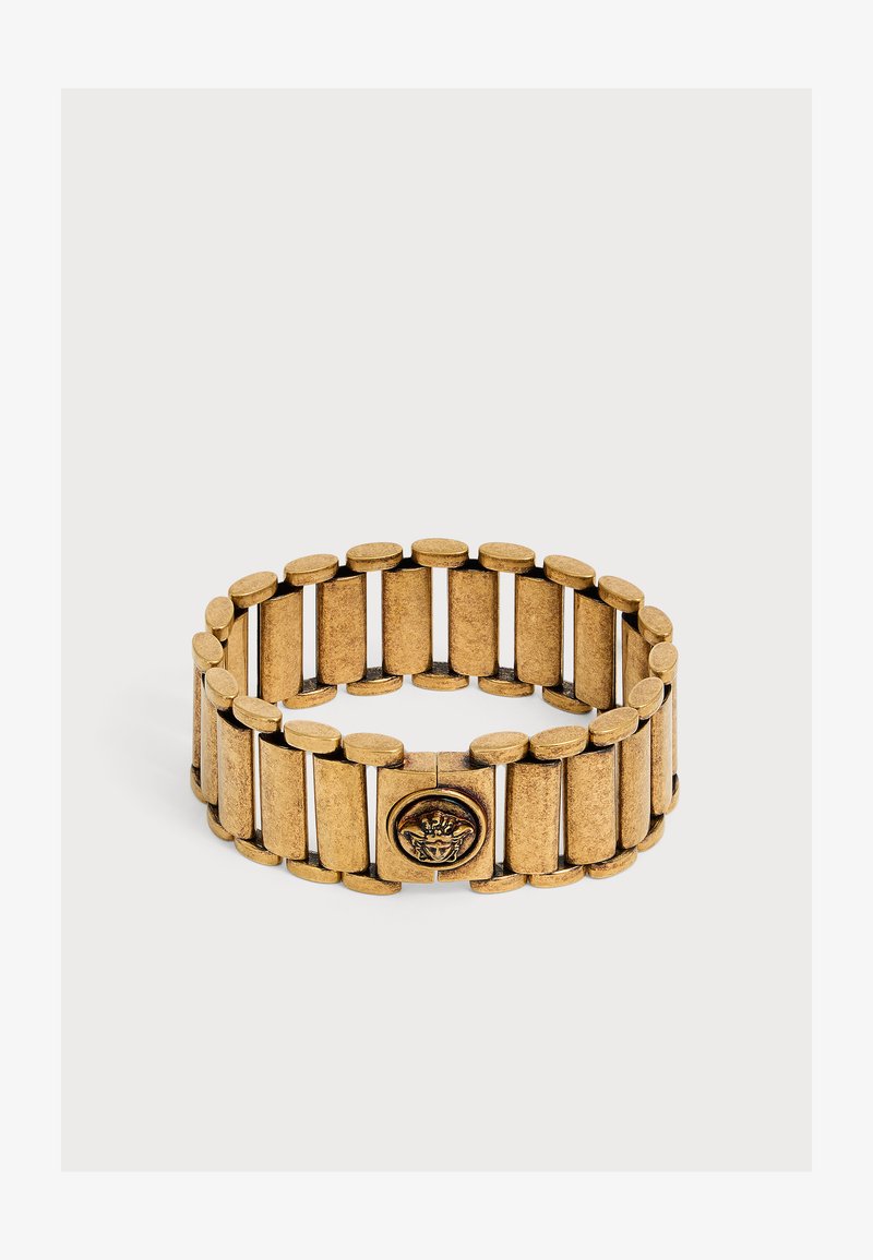 Bracelet en métal couleur or avec de larges maillons rectangulaires et un emblème circulaire représentant un visage au centre.