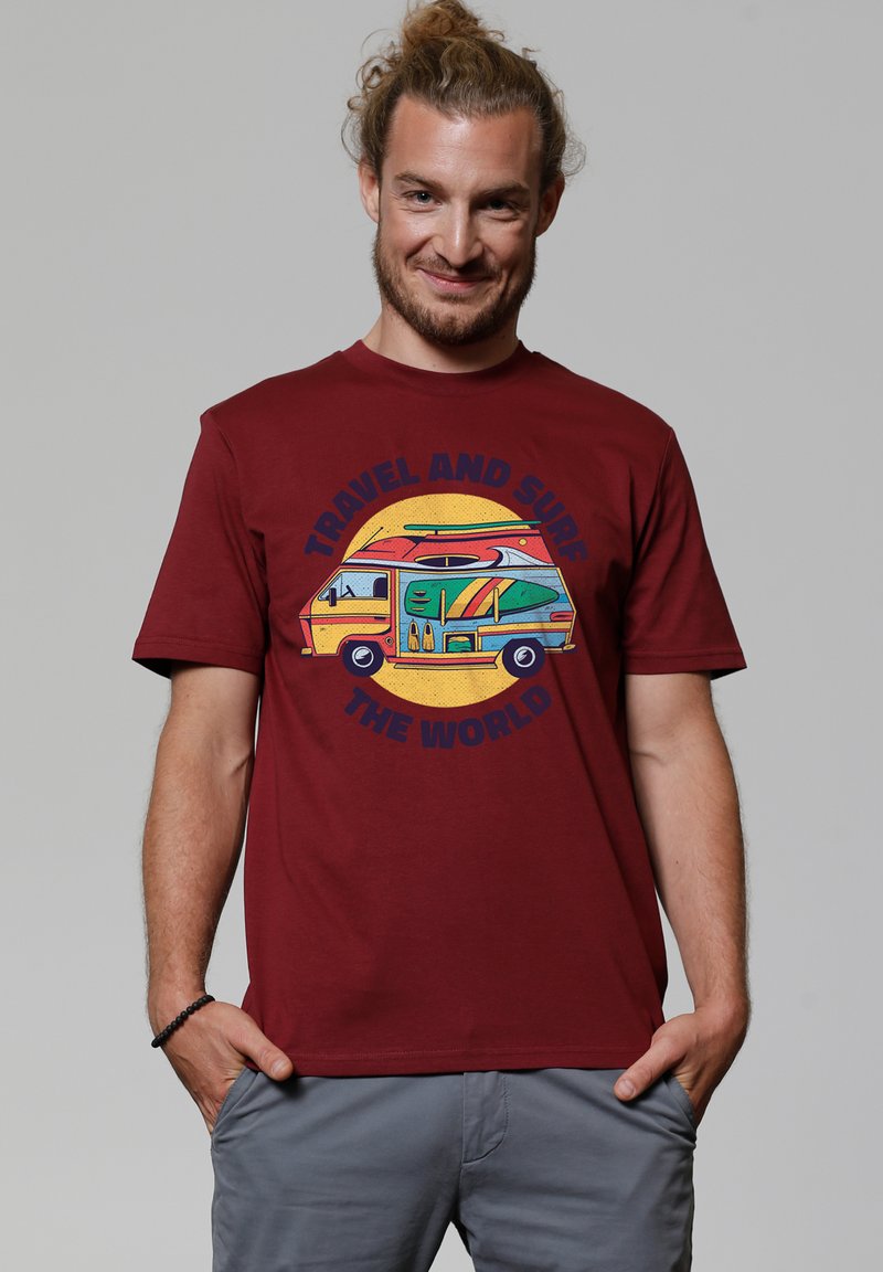 T-shirt bourgogne avec une graphic colorée d'un van aménagé et le texte "VOYAGER ET SURFER LE MONDE" en bleu. Manches courtes, coupe décontractée.