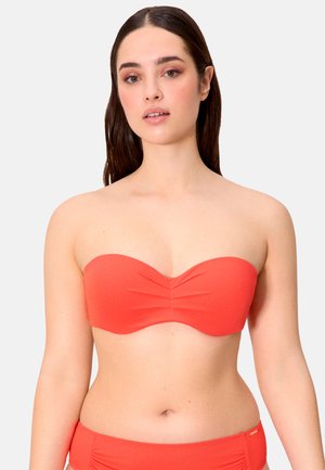 Mujer de cabello largo y castaño, con un bikini coral de top bandeau fruncido y braguitas a juego, sobre un fondo liso.