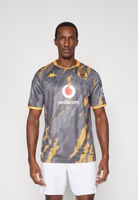 Szürke rövid ujjú futballmez narancssárga díszítésekkel és absztrakt mintákkal. Vodacom és Kaizer Chiefs logókat tartalmaz.