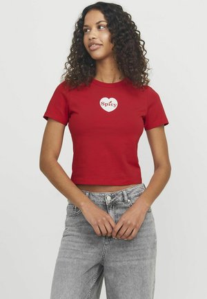 Rode cropped t-shirt met korte mouwen, met een witte hartafbeelding en het woord "Spicy" in een vette lettertype, gecombineerd met grijze jeans.