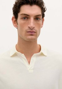 Polo shirt in lichtcrème stof, met een kraag en een knopsluiting en een textuurafwerking. Eenvoudig en minimalistisch ontwerp.