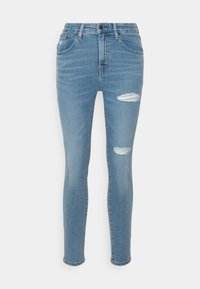 Pantalones vaqueros ajustados en denim azul claro con un lavado desgastado, que presentan desgarros en las rodillas con flecos, un diseño de cinco bolsillos y un cierre de botón en la cintura.