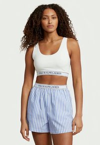 Top scurt alb, cu un bandă branduită, combinat cu pantaloni scurți în dungi albastre și albe, cu șnur și detalii cu nasture.