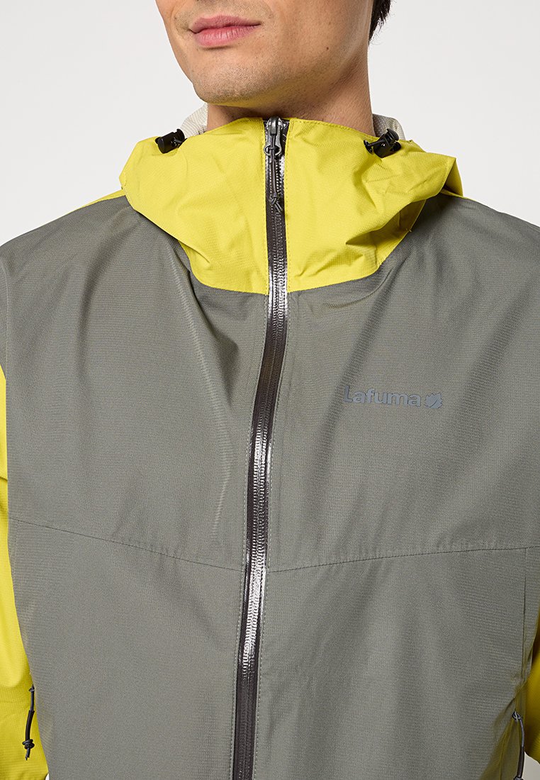 Veste légère grise et jaune avec un zip à l'avant, une capuche ajustable et le logo Lafuma, idéale pour les activités de plein air.