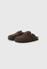 Brown felt clogs with a curved shape, featuring a side buckle, cork insole, and rubber outsole. Soft texture with minimalistic design.