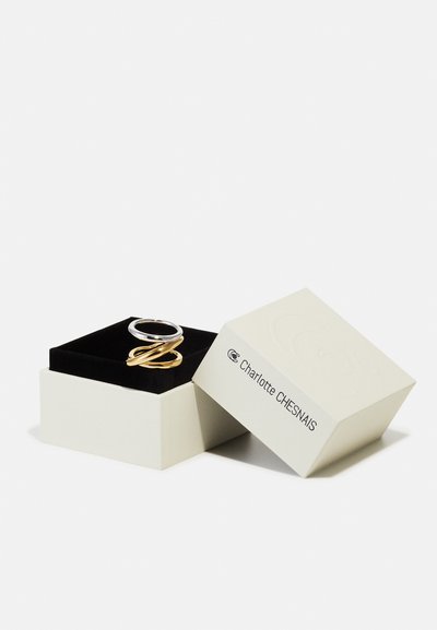 Bagues bicolores en argent et or présentées sur un velours noir dans une boîte à bijoux blanche ouverte Charlotte Chesnais.