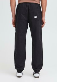 Schwarze Baumwoll-Jogginghosen mit elastischem Bund und Bündchen, ausgestattet mit zwei Gesäßtaschen und einem kleinen Markenlabel an der rechten Tasche.