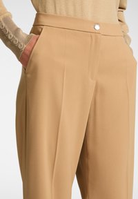 Beiga skräddarsydda byxor tillverkade av mjukt tyg, med sidofickor, en enkel knappknäppning och rak bendesign.