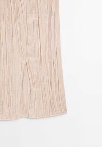 Tissu plissé beige clair avec des plis verticaux et une petite fente près du bas sur fond blanc.