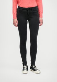 Jeans skinny negros con diseño de cinco bolsillos, con un cierre de botón al frente. Combinados con zapatillas de lona negras y un suéter rosa brillante.