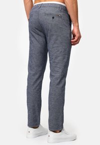 Pantalones de tela texturizada en gris con corte ajustado. Presentan un bolsillo trasero único con botón y costuras de colores. Llevados con zapatillas blancas.