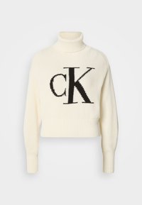 Cremfarbener, gerippter Rollkragenpullover mit abgeschnittenem Saum, der auf der Vorderseite ein großes schwarzes "CK"-Logo trägt. Weiches Strickmaterial, lange Ärmel.
