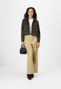Geknipte bruine luipaardprint jas, beige cargo broek met zakken, zwarte handtas en zwarte hoge enkellaarsjes.