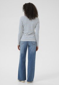 Wit en marineblauwe gestreepte lange mouw shirt, gecombineerd met lichtblauwe wijde jeans. Kenmerkt zich door zachte stof en een klassiek ontwerp.