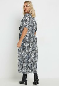 Pitkä, musta-valkoinen käärmeennahkakuosiset mekko, jossa on kapea vyötärö, lyhyet hihat ja hulmuava hame, yhdistettynä mustiin nilkkabooti.