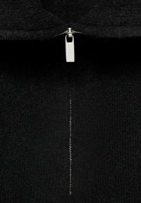Schwarzer Fleece-Stoff mit einem silbernen Reißverschluss, der teilweise geöffnet ist und den Reißverschlusszieher zentriert an der Vordernaht des Kleidungsstücks zeigt.
