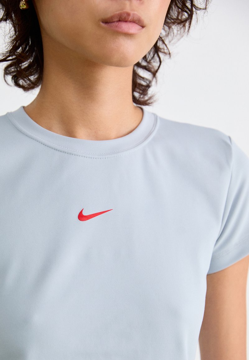 Nahaufnahme einer Person, die ein hellblaues Hemd mit einem kleinen roten Nike-Logo auf der Brust trägt.