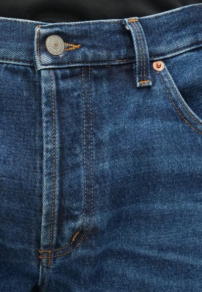 Jean en denim bleu avec un design classique à cinq poches, équipé de ferrures en cuivre, de coutures orange et d'une texture légèrement décolorée.