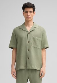Korte mouw, knoopsluiting shirt in een gestructureerde lichtgroene stof, met een borstzak en bruine knopen. Gepaard met bijpassende broek.