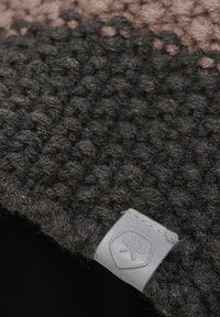 Stickad ullmössa med ett texturerat mönster i mörkgrått och ljusrosa, med en grå logotyppatch på sidan.