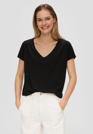 Haut noir à manches courtes en V avec une finition texturée, associé à un pantalon large taille haute de couleur claire. Conception simple et décontractée.