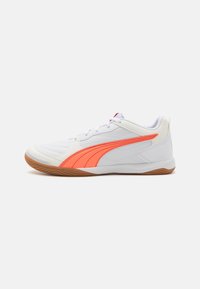 Chaussure de sport blanche avec des accents orange, surface texturée, fermeture à lacets et semelle en caoutchouc. Présente un design épuré et un support rembourré pour la cheville.