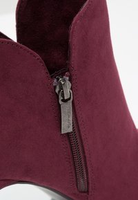 Burgundy mokkanahka nilkkuri, jossa on sileä pinta, sivuvetoketjut ja pyöreä kärki. Sisävuori on vaaleampaa väriä.