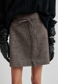 Brun twill minikjol med dragsko i midjan, med ett texturerat mönster. Matchad med långa svarta läderhandskar för kontrast.