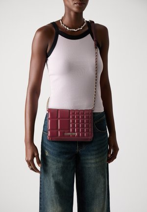 Burgundy quilted crossbody bag with a chain strap and logo detail, complemented by a light tank top and wide-leg denim jeans.