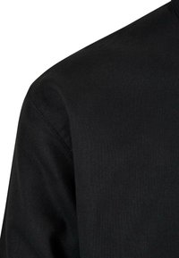 Crna platnena košulja s glatkom teksturom, koja ima okrugli izrez i detalje na ramenu, prikazuje minimalistički dizajn.