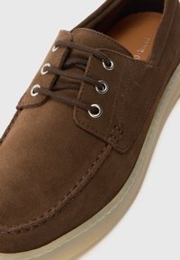 Brune semskede sko med rund tå, snøring, metalløye, og beige gummisåle. Har synlige sømmer og en glatt tekstur.