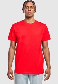 Camiseta de algodón roja con cuello redondo y mangas cortas. Diseño simple con un corte relajado y textura suave, usada por un modelo masculino.