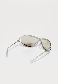 Ochelari de soare cu un design elegant și curbat; cadru metalic argintiu; lentile gri fumurii; pernuțe de nas ajustabile; brațe subțiri cu un finisaj mat.