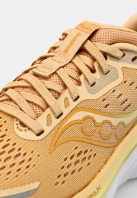 Chaussure de course en mesh orange avec un dessus texturé, des lacets plats et une semelle rembourrée. Présente des éléments de marque et des lignes décoratives dans des teintes plus claires.