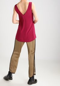 Haut sans manches bordeaux avec un grand dos en V, associé à un pantalon en satin beige avec des rayures noires sur les côtés et des bottines noires.