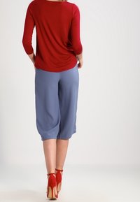 Rode 3/4 mouw top gecombineerd met lichtblauwe cropped broek. Model draagt rode hoge hakken. Zachte stof, relaxte pasvorm, gladde textuur.