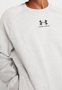 Felpa grigia chiara realizzata in tessuto variegato, con collo rotondo e logo Under Armour nero sul petto.