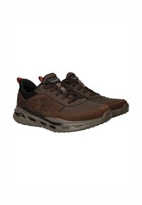 Zapatillas marrones con parte superior de cuero liso, acentos negros, punta redondeada y suela acolchada con grandes bolsas de aire. Diseño con cordones.