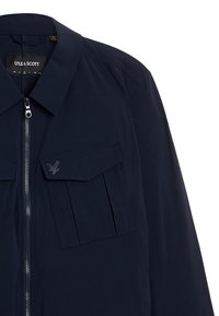 Giacca blu Navy realizzata in tessuto leggero, con chiusura frontale a zip, due tasche sul petto con patte e un dettaglio del logo su una tasca.