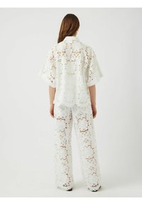 Vit spets tvådelad outfit bestående av en kortärmad topp och vida byxor, båda med blommönster och vågiga kanter.