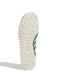 Suela de zapato con un patrón texturizado, que presenta surcos circulares y lineales. La combinación de colores incluye acentos verdes y una base de goma blanca con el logo.