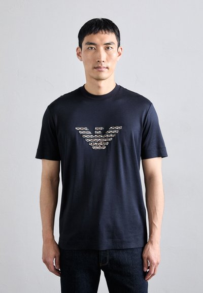 T-shirt en coton bleu marine avec un logo d'aigle graphique à motif contrasté sur la poitrine. Manches courtes et col rond.
