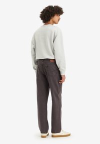 Sweatshirt gris à manches longues, porté avec un pantalon gris foncé. Présente un design simple, une coupe décontractée et un logo discret à l'arrière.