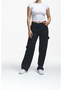 Pantaloni neri a gamba larga con vita alta, dotati di chiusura a bottone e tasche laterali, abbinati a un top attillato bianco a maniche corte.