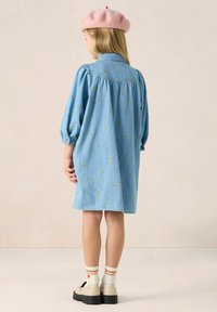 Spijkerjurk met pofmouwen, lichtblauwe kleur, versierd met kleine gele hartjespatronen, gedragen met een roze baret en beige platform schoenen.