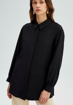Zwarte oversized shirt met een klassieke kraag, lange mouwen gathered bij de manchetten en een gestructureerde stofafwerking.