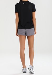 Svart kortärmad träningströja med detalj på sömmen bak, ihop med ljusgrå shorts. Avslutad med ljusgrå träningsskor.